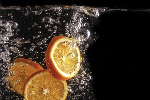 Fette di limone fanno bolle in acqua, fondo nero — Foto Stock