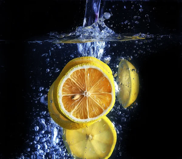 Citronskivor gör bubblor i vattnet, svart bakgrunden — Stockfoto