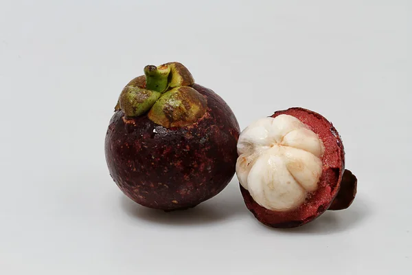 Två Mangostan, halva skalade, vit tillbaka marken — Stockfoto