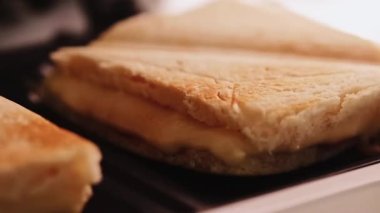 Sandviç tost makinesinde pişirilmiş sıcak üçgen peynirli sandviçler, ev yapımı konforlu yemekler.