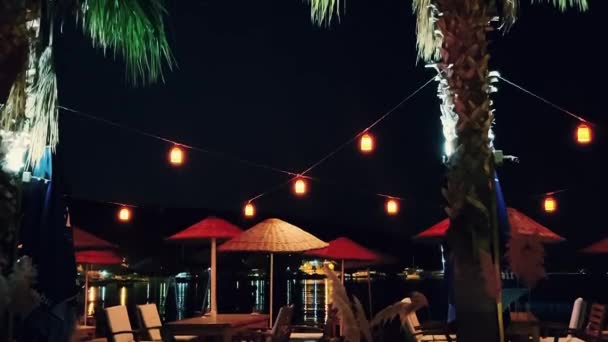 Guarda-sóis de praia, lanternas e palmeiras no resort do hotel à beira-mar na noite de verão, decoração ao ar livre e férias de verão b-roll — Vídeo de Stock