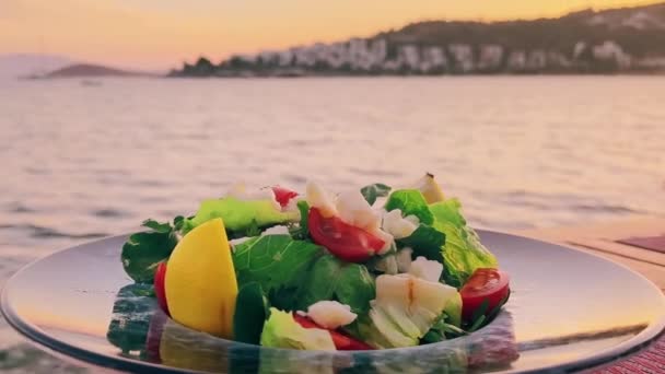 Mediterrane salade met witte kaas en verse groene groenten op bord in een restaurant aan zee bij zonsondergang — Stockvideo