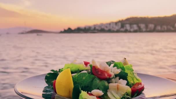 Mediterraner Salat mit weißem Käse und frischem grünen Gemüse auf dem Teller in einem Restaurant am Meer bei Sonnenuntergang — Stockvideo