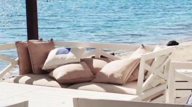 Plaj salonu ve yaz tatili konsepti. Rahat yastıkları, yastıkları ve mavi denizin yanındaki masalı beyaz kanepe.
