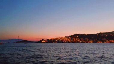 Deniz manzarası, seyahat ve doğa konsepti, deniz dalgaları ve kıyı kasabasının ışıkları gün batımında