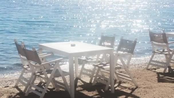 Restauracja plażowa i wakacyjna koncepcja. Białe stoły i krzesła na piasku w pobliżu błękitnego morza w słońcu — Wideo stockowe