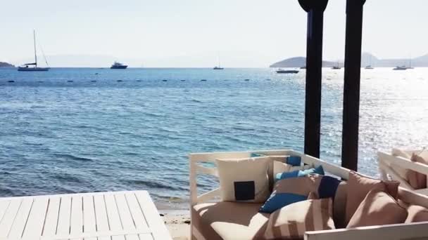 Plážový salonek a letní dovolená koncept. Bílá pohovka s pohodlnými polštáři a polštáři a stůl v blízkosti modrého moře — Stock video