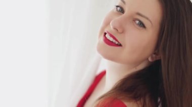 Güzel esmer kadın gülümsüyor, poz veriyor ve dans ediyor, pencereden veya kapıdan parlak bir ışık ve arka planda beyaz perdeler, kadınsı yaşam tarzı ve doğal güzellik.