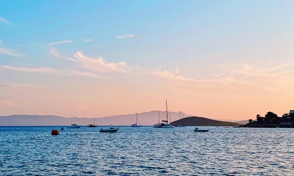 Концепция спокойного мыса и прибрежной природы. Море, лодки, горы и голубое небо над горизонтом на закате — стоковое фото