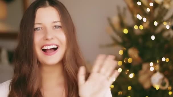 Weihnachts- und Urlaubsgrüße. Glückliche Frau lächelnd und winkende Hand, geschmückte Weihnachtsbaumbeleuchtung im Hintergrund — Stockvideo