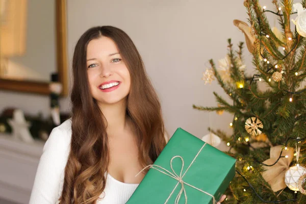 Karácsonyi nyaralás és fenntartható ajándék koncepció. Boldog mosolygós nő tartja csomagolva ajándék környezetbarát zöld csomagolópapír — Stock Fotó