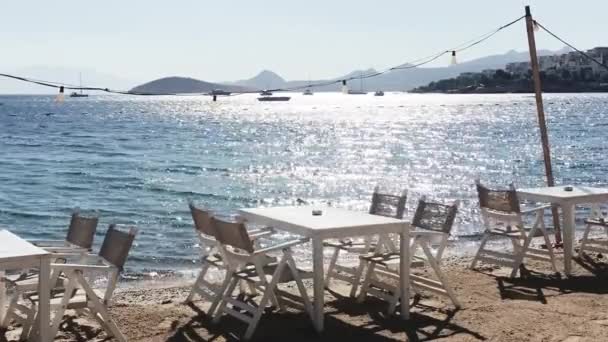 ビーチレストランと夏休みのコンセプト。太陽の光で青い海の近くの砂の上の白いテーブルと椅子 — ストック動画