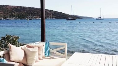 Plaj salonu ve yaz tatili konsepti. Rahat yastıkları, yastıkları ve mavi denizin yanındaki masalı beyaz kanepe.