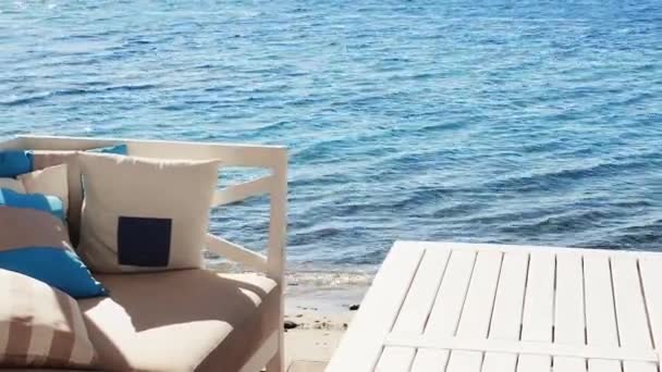 Salon plażowy i letnia koncepcja wakacji. Biała sofa z wygodnymi poduszkami i poduszkami oraz stół w pobliżu błękitnego morza — Wideo stockowe