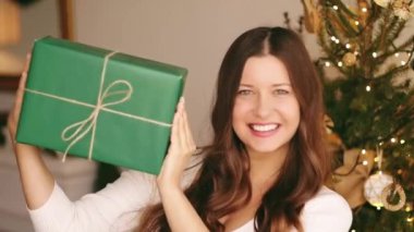 Noel tatili ve çevre dostu hediye konsepti. Elinde sürdürülebilir ambalaj kağıdına sarılı yeşil hediye paketi tutan mutlu bir kadın.