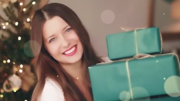 Weihnachtsurlaub und Geschenke für ihr Konzept. Glücklich lächelnde Frau mit verpackten Geschenkschachteln zu Hause, Weihnachtsbaum auf Hintergrund und glitzerndem Bokeh-Effekt — Stockvideo
