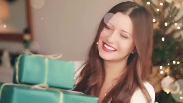 クリスマス休暇と彼女の概念のための贈り物。幸せな笑顔の女性を保持ラッププレゼントボックスで自宅、 xmasツリー上の背景と光沢のある輝きbokeh効果 — ストック動画