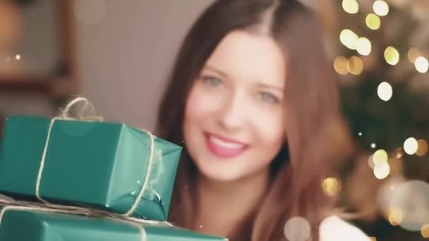 Різдвяні свята та подарунки для її концепції. Щаслива усміхнена жінка тримає загорнуті подарункові коробки вдома, ялинка на фоні і блискучий блиск ефект боке — стокове відео