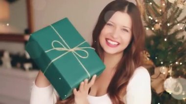 Noel tatili ve konsepti için hediye. Elinde hediye paketi olan mutlu bir kadın, arka planda xmas ağacı ve parlak ışıltılı bokeh efekti. Yüksek kaliteli FullHD görüntüler