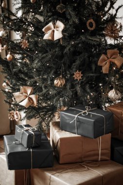 Noel teslimatı ve sürdürülebilir hediye konsepti. Süslü xmas ağacının altında geri dönüşümlü kağıtla birlikte çevre dostu paketlere sarılmış siyah hediye kutuları.