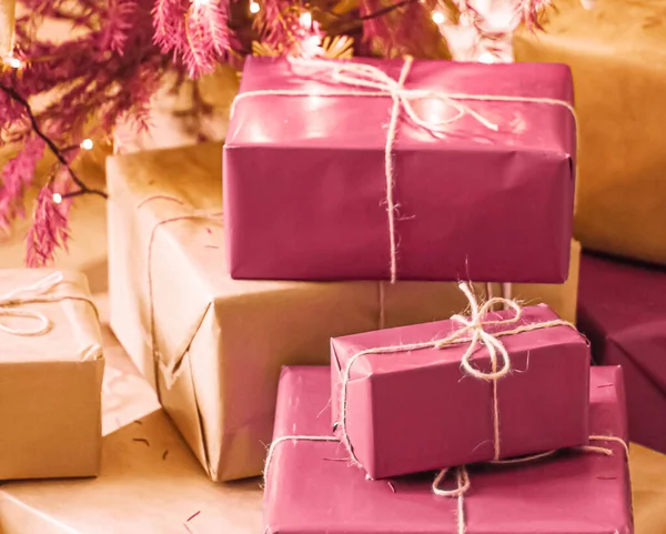 Entrega navideña y concepto de regalos sostenibles. Cajas de regalo rosadas envueltas en un embalaje ecológico con papel reciclado bajo un árbol de Navidad decorado —  Fotos de Stock