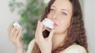 Güzel gülümseyen genç bir kadın açık yüz kremi kavanozunu tutuyor, doğal güzellik olarak organik kozmetik ürünü ve günlük sağlıklı cilt bakımı rutini, lüks kozmetik ürünleri, insanlar ve sağlık reklamı.