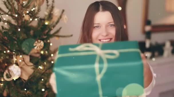 Vacanze di Natale e regalo per il suo concetto. Felice donna sorridente in possesso di scatola regalo avvolto a casa, albero di Natale su sfondo e scintillante effetto bokeh glitter — Video Stock