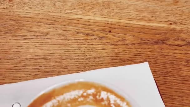 Pausa para el café y concepto de humor romántico. Copa de capuchino de caramelo con arte de espuma en forma de corazón hecho de leche sin lactosa, servido en la mesa de madera en la cafetería — Vídeo de stock
