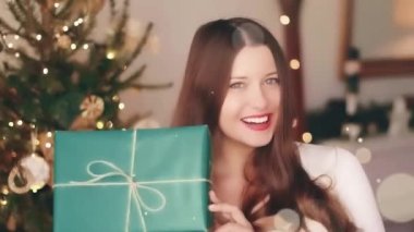 Noel tatili ve konsepti için hediye. Mutlu gülümseyen kadın hediye paketini evde tutuyor, arka planda xmas ağacı ve parlak parlak ışıltı efekti