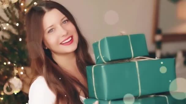 クリスマス休暇と彼女の概念のための贈り物。幸せな笑顔の女性を保持ラッププレゼントボックスで自宅、 xmasツリー上の背景と光沢のある輝きbokeh効果 — ストック動画