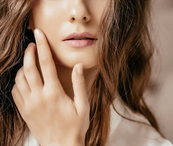 Hermosa mujer que aplica cosméticos con la mano en la cara, aspecto natural y peinado largo ondulado, retrato de belleza y rutina de cuidado de la piel — Foto de Stock