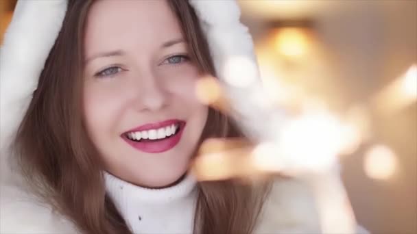 Vacances d'hiver et Noël concept de célébration. Belle femme souriante en fourrure pelucheuse blanche tenant des étincelles brûlantes, portrait de Noël festif — Video