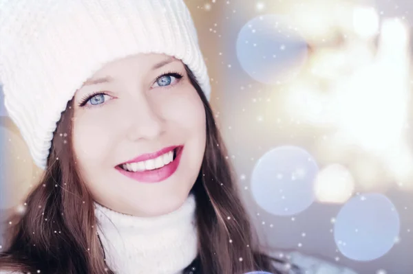 Natal, pessoas e conceito de férias de inverno. Feliz sorrindo mulher vestindo chapéu de malha branco como close-up xmas rosto retrato, brilho de neve e efeito bokeh — Fotografia de Stock