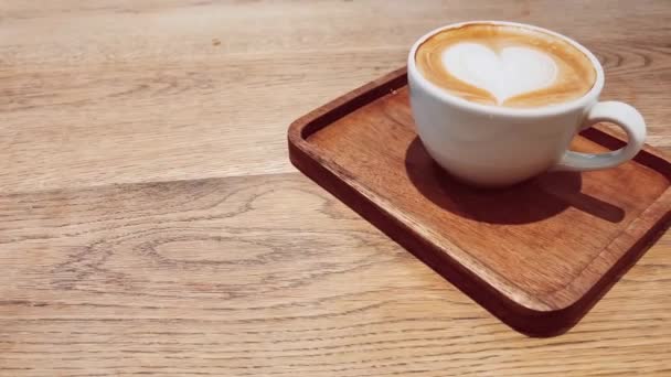 Coffee break and romantic mood concept. Cup of caramel cappuccino with heart shaped foam art made of lactose-free milk, served on wooden table in cafeteria — Stock Video