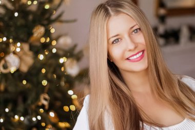 Noel zamanı ve tatil ruh hali konsepti. Mutlu gülümseyen kadın ve arka planda süslü Noel ağacı ışıkları.