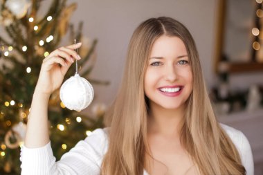 Noel dekorasyonu ve tatil ruh hali konsepti. Mutlu, güler yüzlü bir kadın Noel ağacını şenlikli oyuncaklar ve süslemelerle süslüyor.