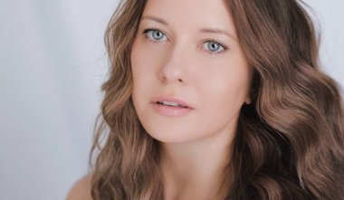 Güzellik, saç bakımı ve doğal makyaj. Uzun açık kahverengi dalgalı bukleli güzel bir kadın. Saç stili, kusursuz bir cilt ve organik kozmetik makyaj. Yumuşak odaklı bir portre.