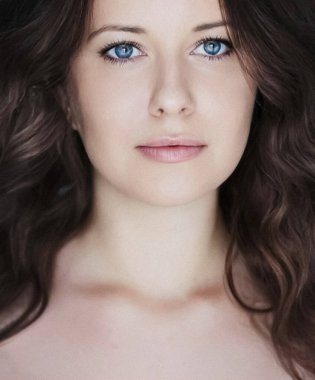 Güzellik, saç stili ve doğal makyaj. Uzun kıvırcık saçlı güzel bir kadın, kusursuz bir cilt ve organik kozmetik makyaj, yumuşak odaklı bir portre ve geçmişe dönük film tahıl etkisi.