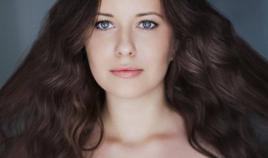 Güzellik, saç stili ve doğal makyaj. Uzun kıvırcık saçlı güzel bir kadın, kusursuz bir cilt ve organik kozmetik makyaj, yumuşak odaklı bir portre ve geçmişe dönük film tahıl etkisi.