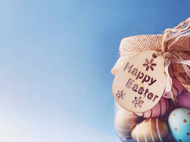 Mutlu Paskalyalar. Mavi arka planda cam kavanozda renkli Paskalya yumurtaları, Hıristiyan dini ve tatil konsepti