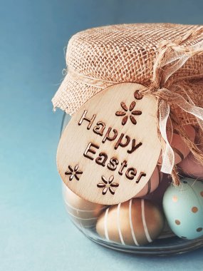 Mutlu Paskalyalar. Mavi arka planda cam kavanozda renkli Paskalya yumurtaları, Hıristiyan dini ve tatil konsepti