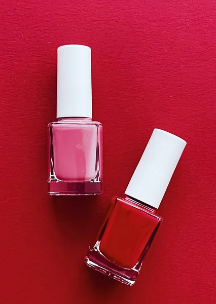 Red and pink nail polish bottles on red background, manicure and beauty cosmetics concept