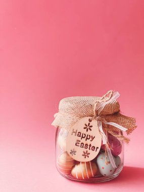 Mutlu Paskalyalar. Pembe arka planda cam kavanozda renkli Paskalya yumurtaları, Hıristiyan dini ve tatil konsepti