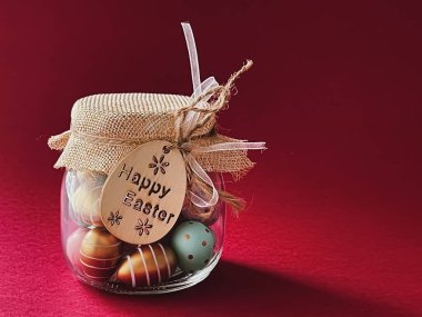 Mutlu Paskalyalar. Kırmızı arka planda cam kavanozda renkli Paskalya yumurtaları, Hıristiyan dini ve tatil kavramı