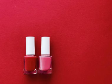 Kırmızı arka planda kırmızı ve pembe oje şişeleri, manikür ve güzellik kozmetik konsepti