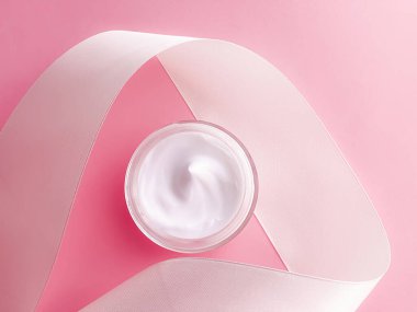 Cilt kremi kozmetik ürünleri, yüz kremi kavanozu ve pembe arka planda beyaz ipek kurdele.