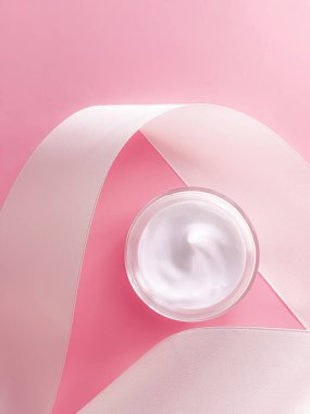 Cilt kremi kozmetik ürünleri, yüz kremi kavanozu ve pembe arka planda beyaz ipek kurdele.