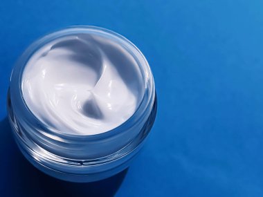 Mavi arka planda ürün örneği olarak yüz kremi kavanozu, güzellik ve cilt bakımı, kozmetik bilimi konsepti