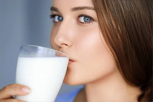 Happy young woman drinking milk or protein cocktail from glass, healthy drink, diet and wellness concept