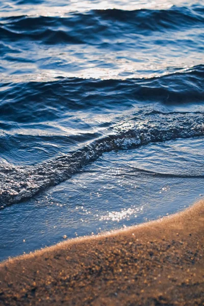 Blue sea waves and golden sand in sunshine glow at sunset, sandy beach and coastal nature concept